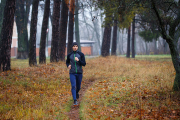 Fototapeta premium Young running man in fall park. Jogging in cold and misty weather