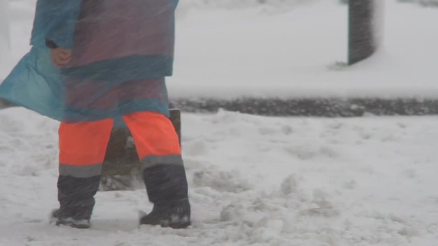 Winter. A worker with a shovel in overalls clears snow falling during a snowfall. Winter collapse on the streets of the city. Legs close-up