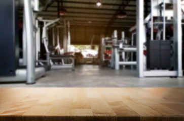 Wooden table on blurred background of fitness gym interior of modern club with equipment for your photomontage or product display.