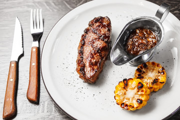 Beefsteak with grilled corn and sauce on white plate