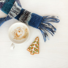 warming winter coffee break/ white mug with frothy cappuccino, blue scarf and ginger fir tree top view 