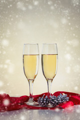 Two glasses with champagne, red ribbon and fir cones. Snowfall