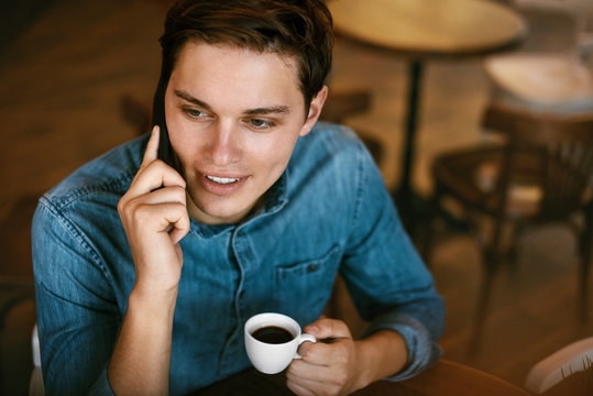 Man Talking On Phone And Drinking Coffee In Cafe.