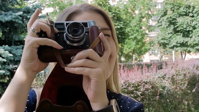 Closeup slow motion footage of young woman making photo on old manual camera at park