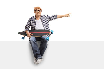 Old hipster with a longboard sitting on a panel and pointing