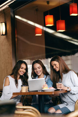 Friends In Cafe. Beautiful Smiling Girls Using Tablet.