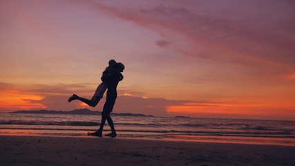 Silhouette of happy loving couple meet and play at the beach on sunset in ocean shore