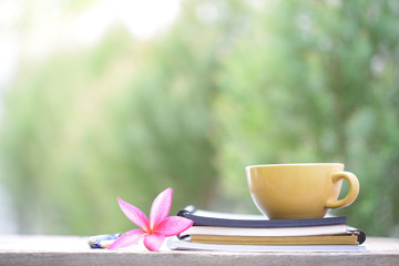 Yellow coffee cup with flower and notebook on wooden table