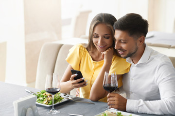 Couple In Love Looking On Phone Having Dinner In Restaurant.