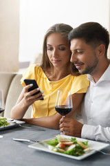 Couple In Love Looking On Phone Having Dinner In Restaurant.