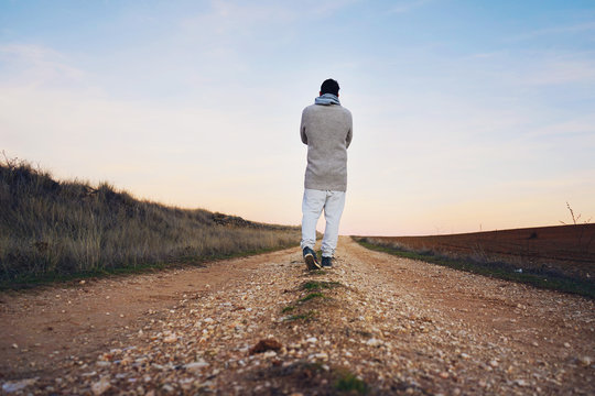 Hombre joven caminando por un camino de tierra al atardecer 