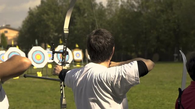 Male archer concentrating and shooting after some seconds, other competitors around.