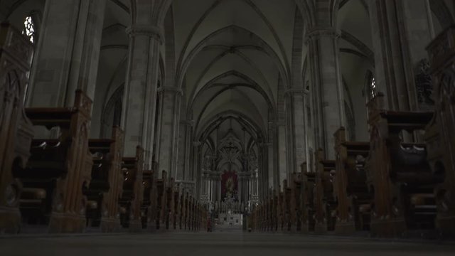 Long, large church hallway in the darkness, vaults on high and benches at both sides.