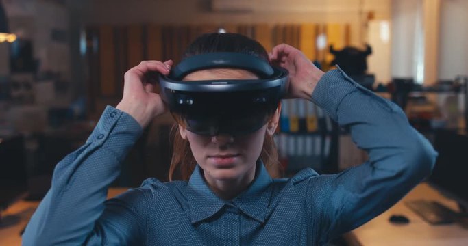 Young Caucasian female professional puts on augmented reality AR hololens headset in modern office. 4K UHD