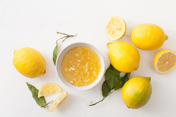 Fresh lemons with leaves and chopped lemons and sugar in a bowl on a white background.