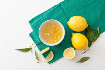 Fresh lemons with leaves and chopped lemons and sugar in a bowl on a white background.