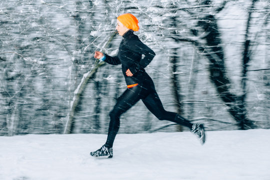 Young woman running outdoors on a cold winter day in snowfall evening time. Motion blurred image