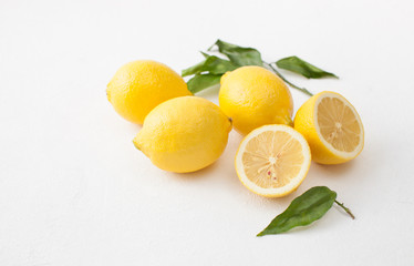 A bunch of lemons with leaves and sliced lemons on a white concrete background.