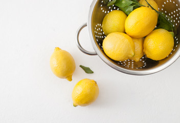 Fresh lemons with leaves in a colander on a white concrete background.