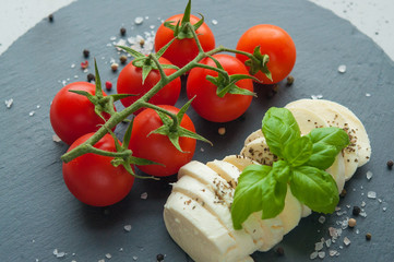  mozzarella cheese with basil and cherry tomatoes on a stone table