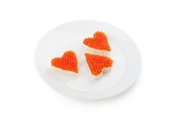 Three sandwiches with red caviar in the shape of heart lie on a white plate isolated on white background.