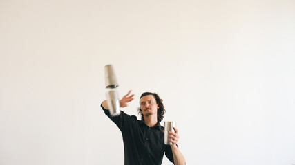Professinal bartender man juggling bottles and shaking cocktail at mobile bar table on white...