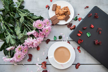 A Cup of coffee,note book , cracker, cookie, biscuit, lupins flowers on a wooden table.