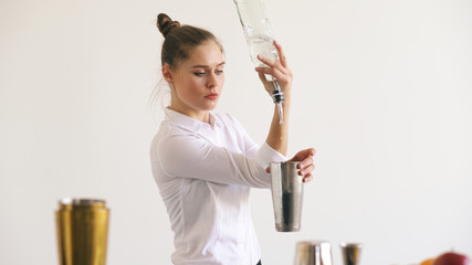 Professinal bartender girl juggling bottles and shaking cocktail at mobile bar table on white background