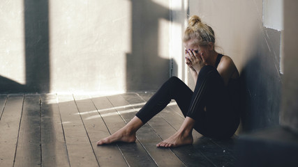 Closeup of young teenage girl dancer crying after loss perfomance sits on floor in hall indoors