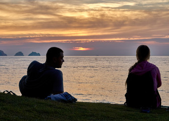 Young couple sitting on the beach and watching sunset