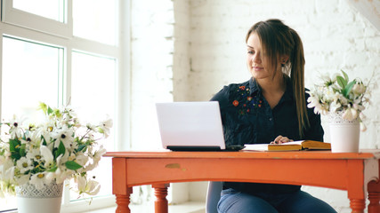Young beautiful woman student sitting with laptop and writing book at cafe indoors