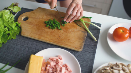 Closeup of girl hands cutting green onion on wooden board for pizza in the kitchen at home