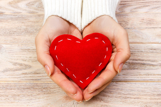 red heart in hands closeup on wooden background