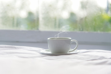 Fresh morning coffee on the white bed near window in the sunny day, green nature background.  Lifestyle Concept