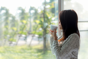 Asian woman fresh morning drinking coffee and looking out of the window on sunny day. Copy Space.  Lifestyle Concept.