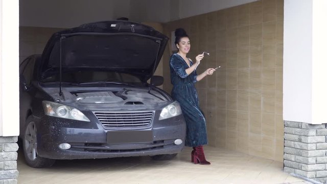 Beautiful woman with wrenches sits at the hood of car