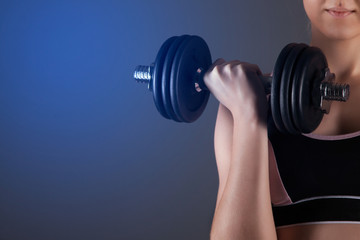 Fototapeta na wymiar A sporty girl holds a dumbbell in her hands, shakes a muscular. Against a dark background
