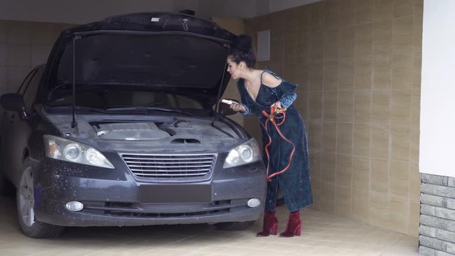 Young woman try to connect jumper cables with car engine