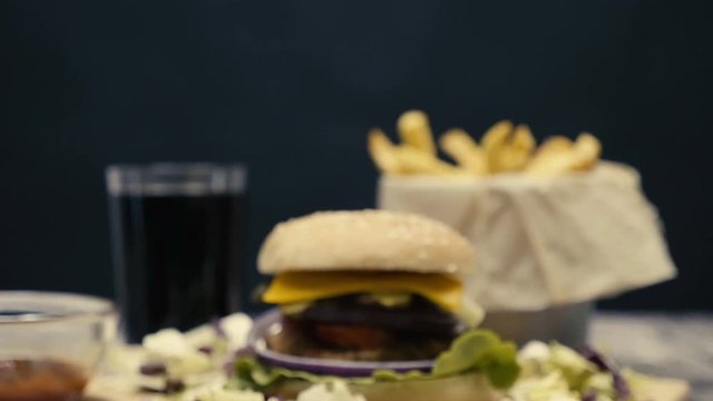 Zoom in on fast food dinner made of hamburger with fries on wooden table. Fast food cheeseburger made with fresh meet and salad ingredients on a plate next to golden french fries.