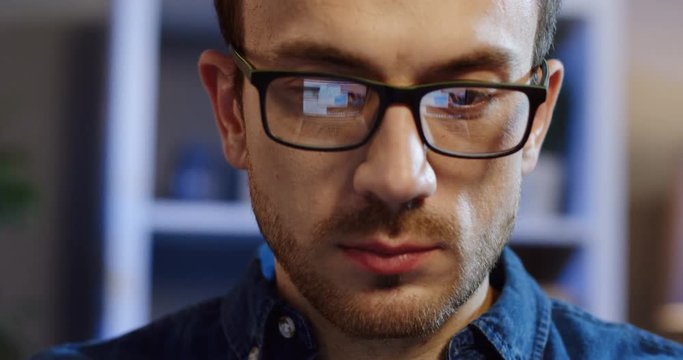 Close up of the caucasian attractive man's face in glasses while he working on the computer at home in the evening. Portrait. Inside