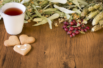 Healthy concept of dry red rose hips, cup of herbal tea and dry sideritis scardica and linden flowers on wooden background.