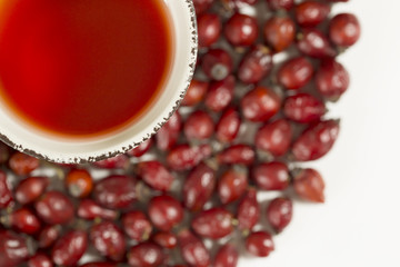 Dry Rose Hips with cup of hot tea on white background. Focus on the glass. Top view, macro, close up.