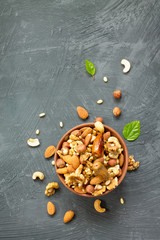 Various nuts in a ceramic bowl (walnut, cashew, almonds, pine nuts, hazelnuts) on a gray stone or slate background. The concept of a healthy dessert. Flat lay, top view with copy space.