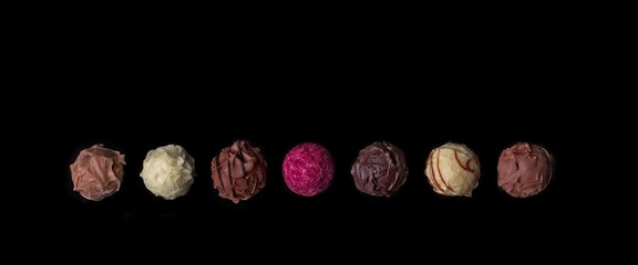 Verschiedene Schokoladentrüffel in einer Reihe - Isoliert auf schwarzem Hintergrund. 