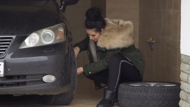 Young stylish woman unscrew the nuts on car wheel