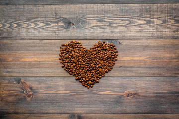 Coffee beans in heart shape on dark wooden table top view copyspace. Coffee background.