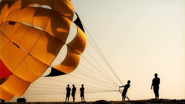 Silhouettes of people on the beach. They inflate the parachute.