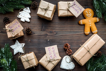 Gift exchange. Boxes with note Santa Secret near spruce branch and gingerbread cookies on dark...