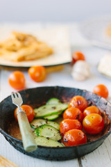 Roasted cherry tomatoes and cucumbers in frying pan.