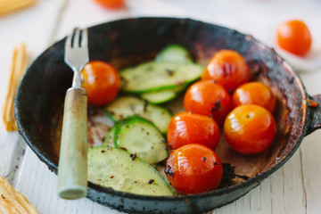 Roasted cherry tomatoes and cucumbers in frying pan.